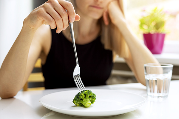 Woman eating single broccoli stalk on plate