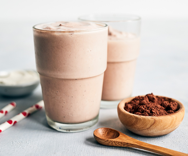 Two glasses of Tiramisu Shakeology smoothie with Café Latte Shakeology and cocoa powder and red and white straws.