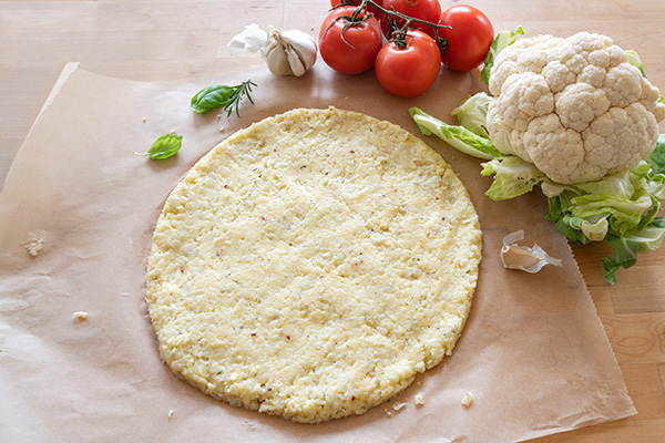 pizza crust from shredded cauliflower on baking paper.