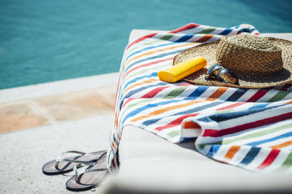 Sunscreen, hat, sunglasses on a towel by the pool