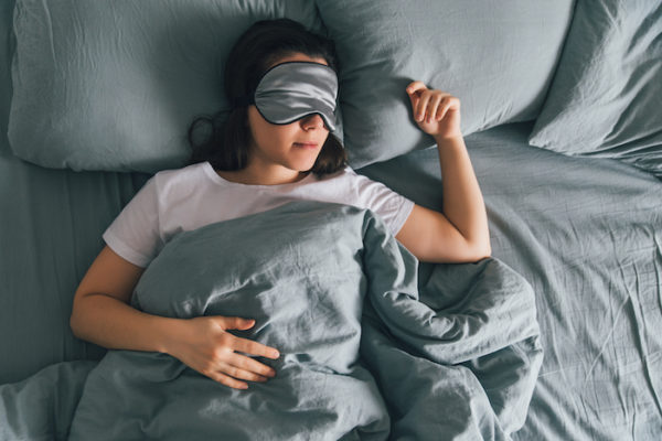 mujer duerme con parche en el ojo en la cama gris | dia de descanso