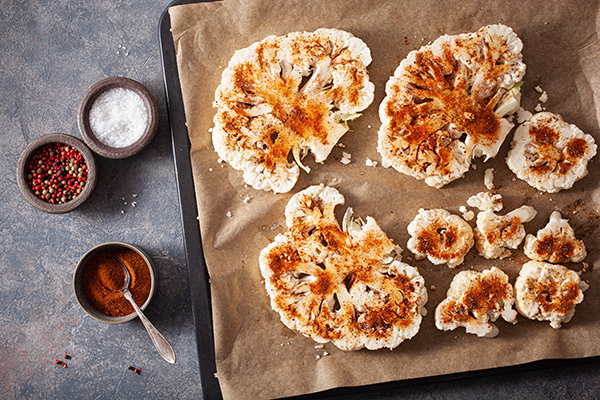 Raw cauliflower steaks with spices on baking sheet. 