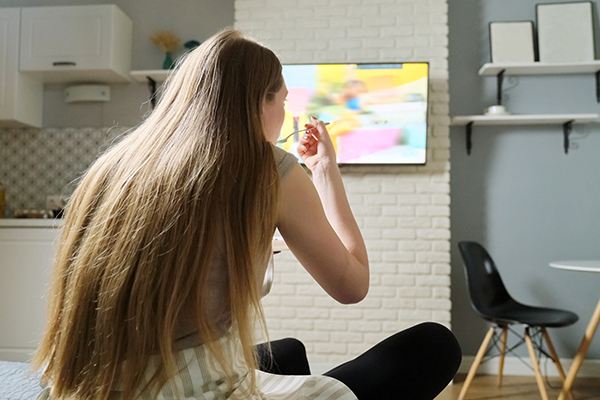 Young woman sitting at home watching tv and eating
