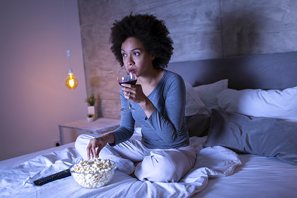 Woman eating popcorn, drinking wine in bed
