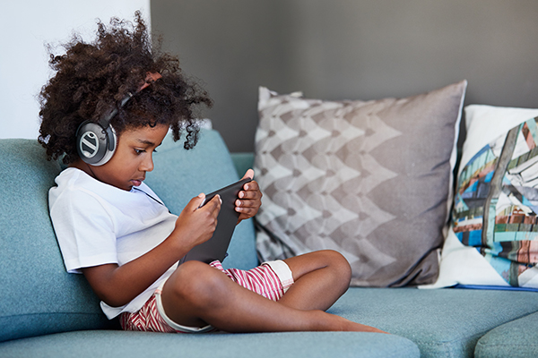 Boy sitting on couch with headphones and tablet