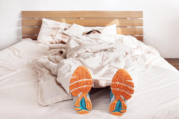Woman lying in bed with running shoes on