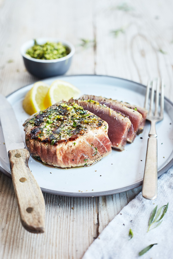 Herb and Garlic Grilled Tuna Steaks with lemon on a platter with fork and knife on a wooden table.