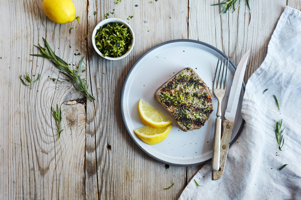 Herb and Garlic Grilled Tuna Steaks with lemon on a platter with fork and knife on a wooden table.