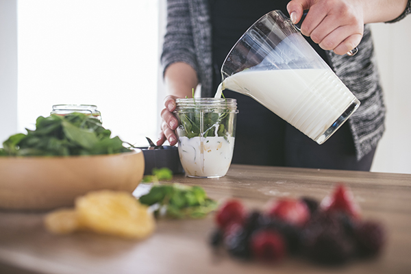 Making a smoothie with spinach, milk, and fruit