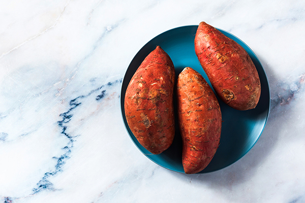 three sweet whole raw orange potatoes on marble table