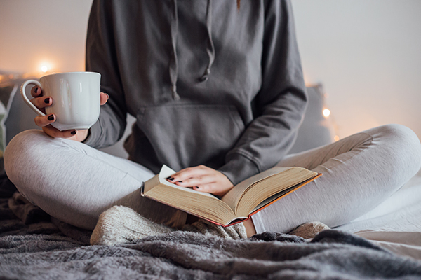 Girl holding cup of hot tea and reading in bed. 