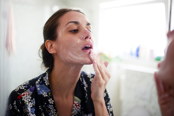 Woman using cleanser on her face at home