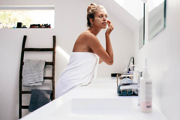 Woman applying facial lotion in front of bathroom mirror