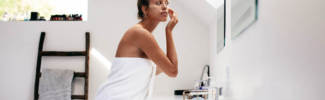 Woman applying facial lotion in front of bathroom mirror