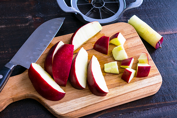 Slicing a red apple into chunks on a wood cutting board