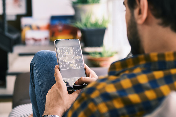 Young Man Playing Sudoku Game With App On Smartphone