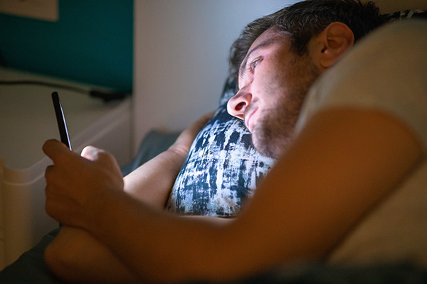 Young man lying in bed at night and using his smart phone