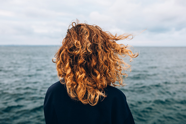 View from the back a woman with curly hair looks at the sea