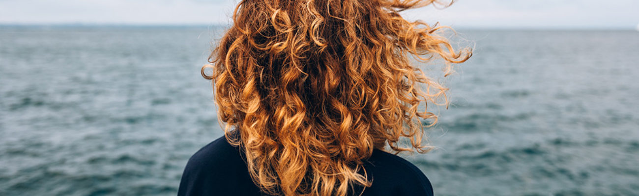 View from the back a woman with curly hair looks at the sea