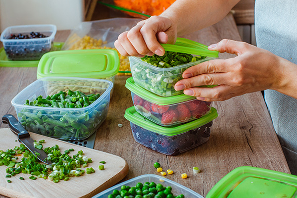 Woman putting fruits, vegetables into plastic containers