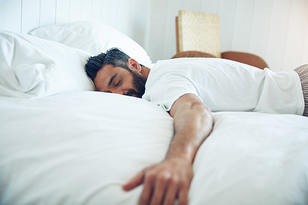 Man lying face down in bed, sleeping.