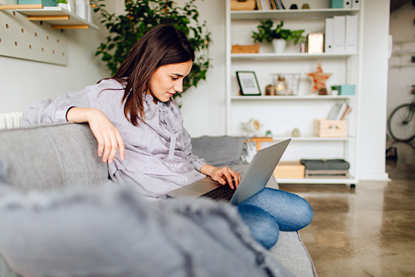 Woman using computer at home on couch.