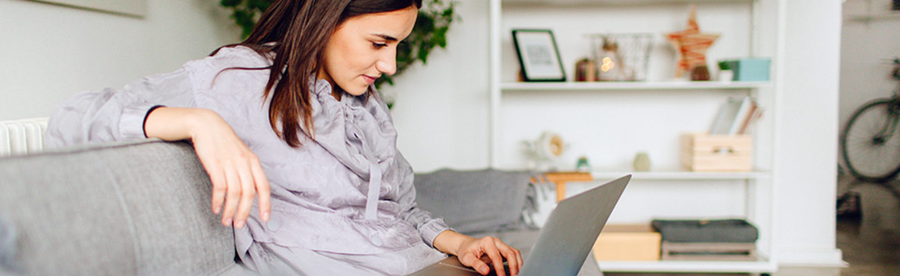 Woman using computer at home on couch.