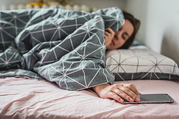 A young woman waking up to smartphone alarm.