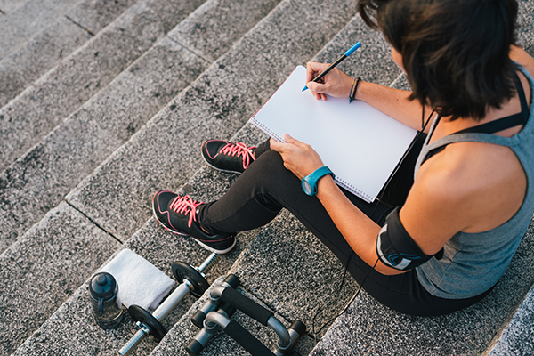 Woman writing in fitness journal outside