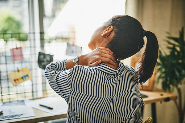 Woman rubbing her neck while working from home