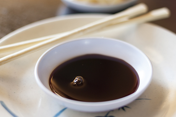 Bowl of soy sauce with chopsticks on table