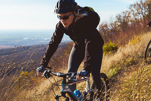 Woman mountain biker ascends meadow.