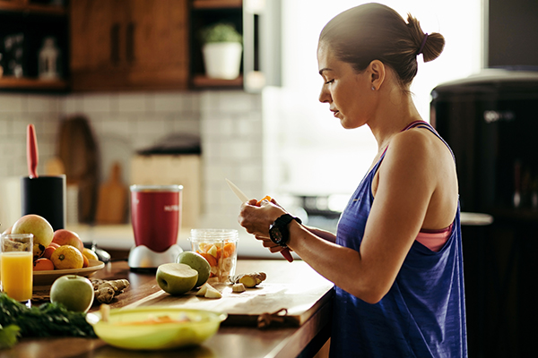 Woman making a healthy smoothie and slicing fresh fruit in the kitchen.