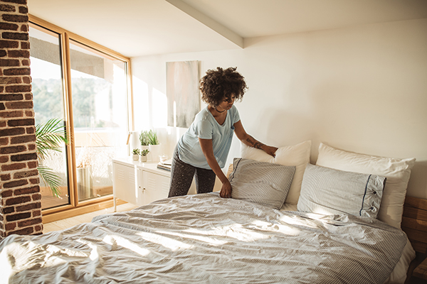 Young woman making bed at home.