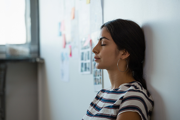 Tired young woman leaning on wall in a office