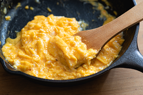 Scrambled eggs cooked in an cast iron skillet, wooden spatula.