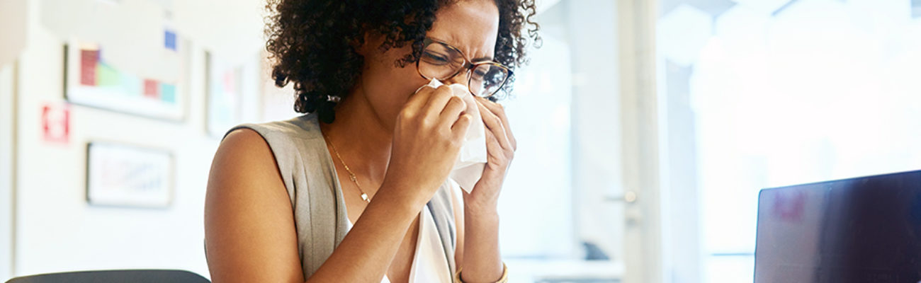 Woman at desk sneezing from allergies