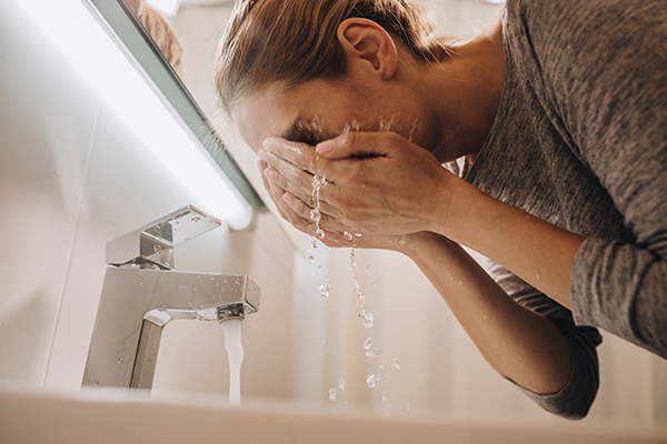woman washing her face in her bathroom.
