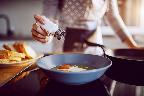 Woman shaking salt into bowl of eggs