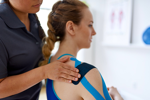 Woman apply KT tape to athlete's shoulder
