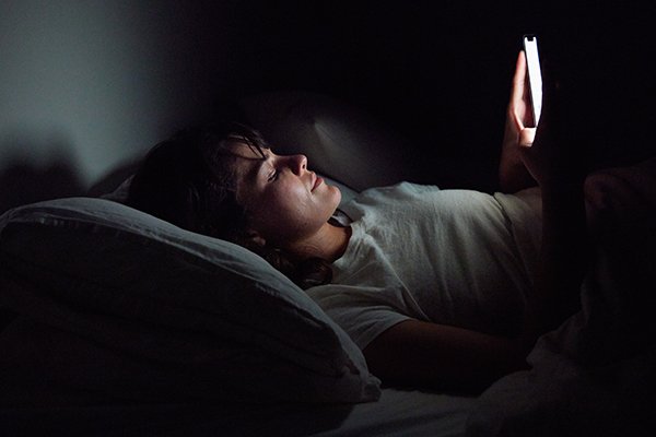 Woman lying in bed at night with her face illuminated by her cellphone.