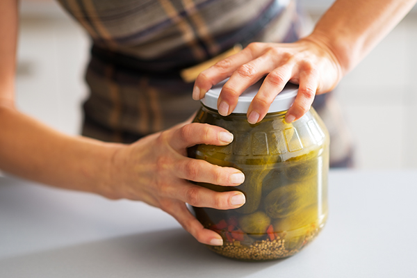 Closeup of womans hands opening a large pickle jar