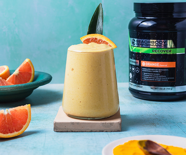 Pineapple Orange Turmeric Smoothie in a glass, tub of Beachbody Performance Recover