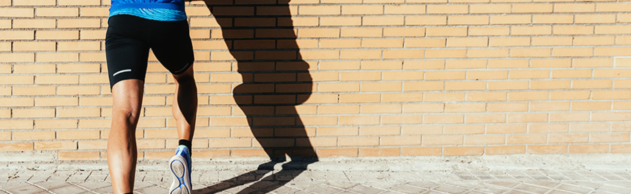 Back view of man stretching ankle, calf against wall