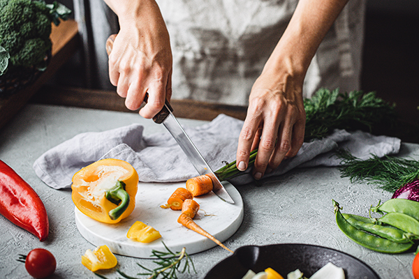 نمای نزدیک از دستان زن در حال خرد کردن سبزیجات روی پیشخوان آشپزخانه.