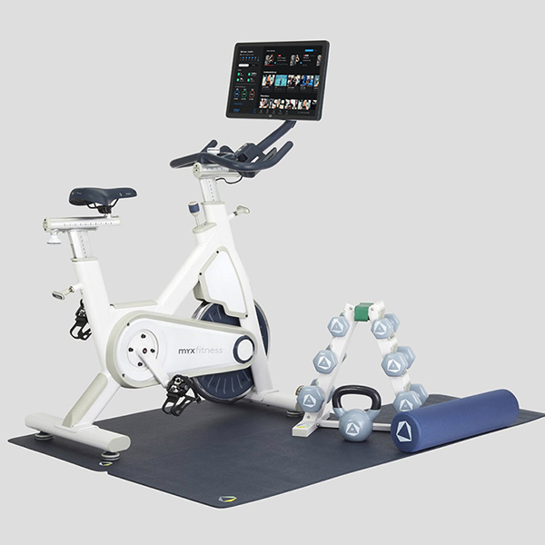 White Beachbody bike by MYX on stabilizing mat with weight rack