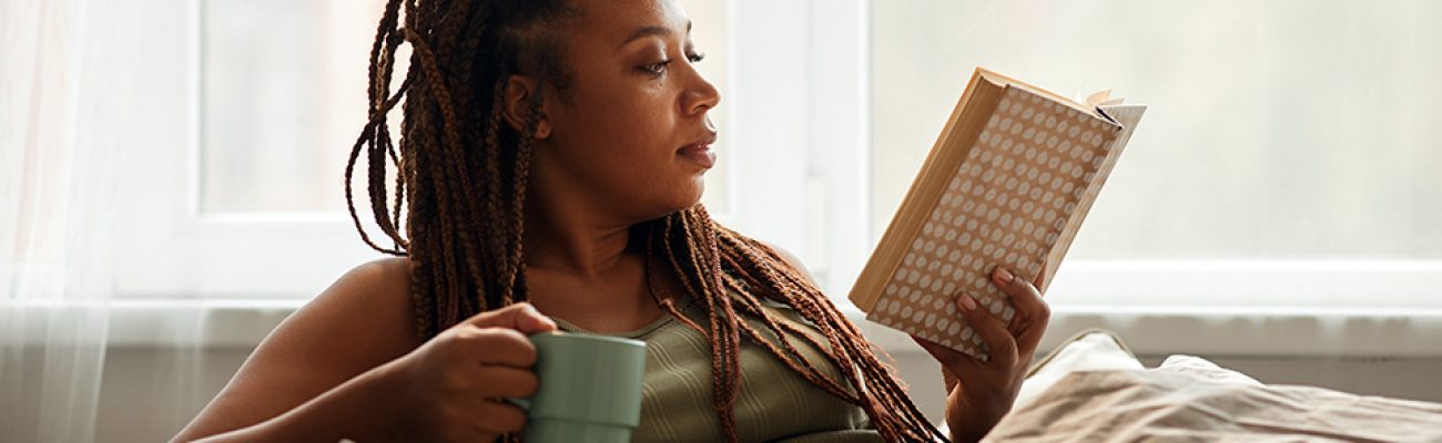 Woman sitting on a couch reading a book, drinking tea