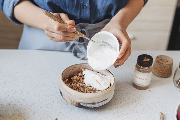 Hands spooning Greek yogurt over granola