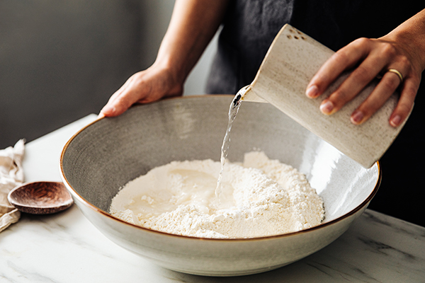 Woman pouring water into a bowl of flour