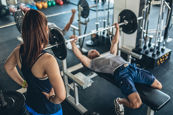 Woman trainer spotting man doing bench press